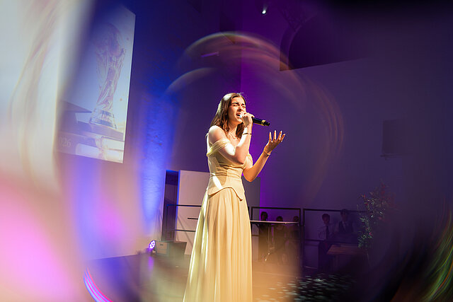 Gesangsauftritt im Abendkleid auf der Abiball-Bühne in violetter Lichtstimmung