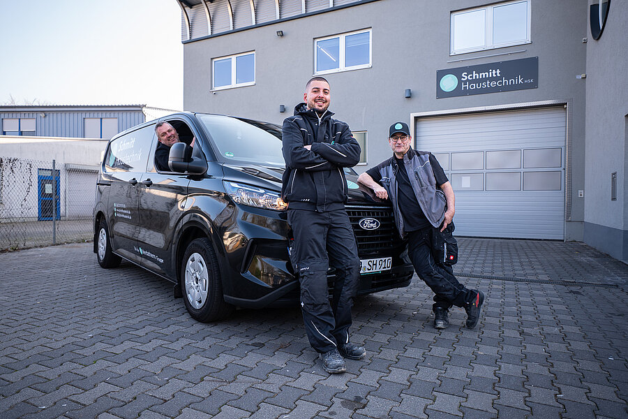 Drei Monteure von Schmitt Haustechnik am Firmentransporter vor der Halle