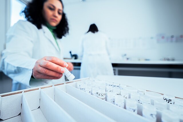 Laborantin nimmt ein Probenröhrchen aus dem Probenkarton, Labordreh für die Academia-Gruppe in Heidelberg
