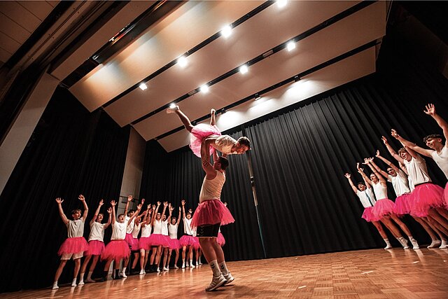 Bühnenshow beim Abiball — Tänzerinnen in pinken Tutus mit Hebefigur auf der Bühne