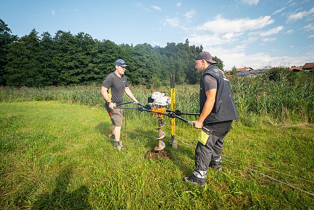 Zwei Zaunteam-Monteure bohren mit dem Zweimann-Erdbohrer ein Pfostenloch im Chiemgau