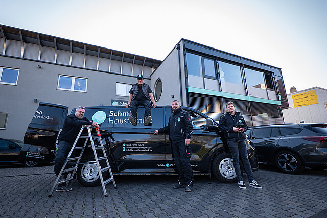 Team von Schmitt Haustechnik am beschrifteten Firmentransporter, ein Mitarbeiter auf dem Dach, daneben eine Stehleiter
