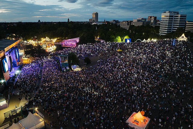 Luftaufnahme von DAS FEST Karlsruhe bei Dämmerung: Menschenmenge mit Handylichtern vor der Hauptbühne