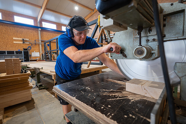 Zimmerer mit Schutzbrille und Gehörschutz an einer großen Holzbearbeitungsmaschine bei Bauer Holzbau