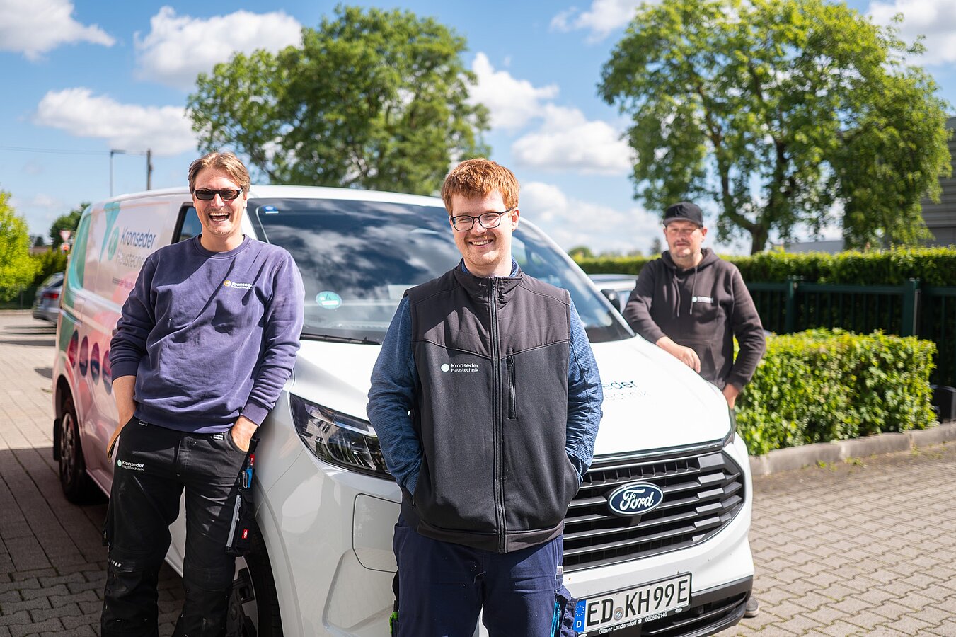 Drei Monteure lachen vor dem gebrandeten Firmentransporter