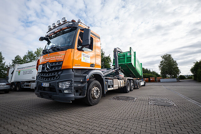 Oranger Abrollkipper der Werner Wiederhold GmbH mit Container auf dem Betriebshof