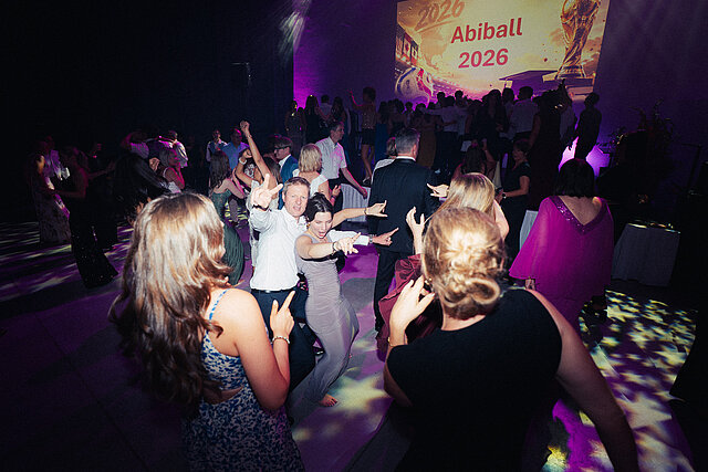 Volle Tanzfläche in violettem Licht, Gäste tanzen vor der Leinwand Abiball 2026, Sternenmuster auf dem Boden